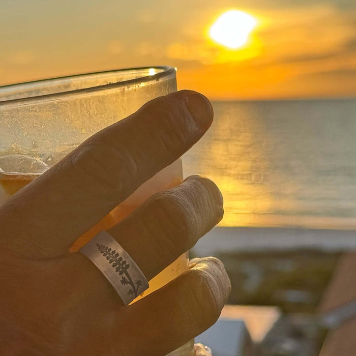 Hand holding a drink at sunset, showcasing the Lupine Adjustable Ring with simple silhouette of a lupine flower.
