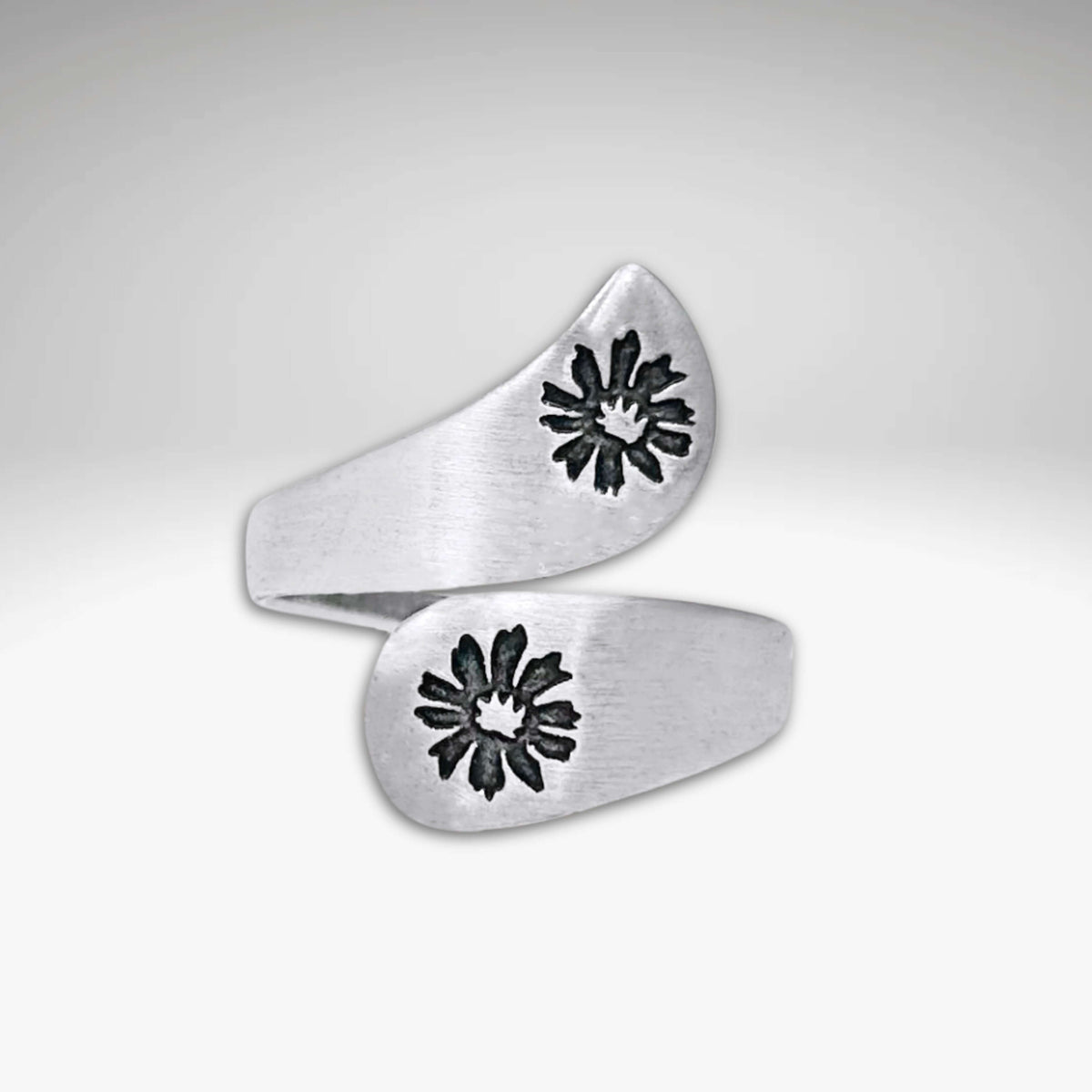 The Bitterroot Bypass Adjustable Ring is a silver wrap-around band with a brushed finish and two bitterroot flower designs at each end.