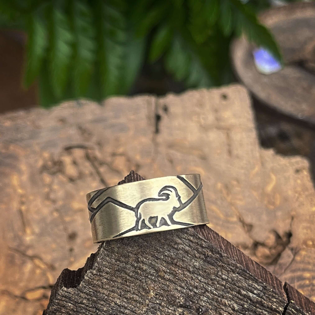 Mountain Goat Adjustable Ring featuring goat design on antique brass finish, set on wooden surface with greenery.