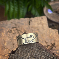 Mountain Goat Adjustable Ring featuring goat design on antique brass finish, set on wooden surface with greenery.
