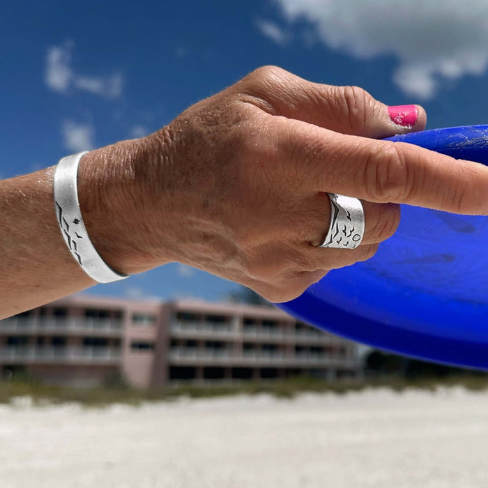 Flyover Adjustable Ring with Mountains, Waves, Full Moon and Birds worn on a hand holding a blue frisbee.