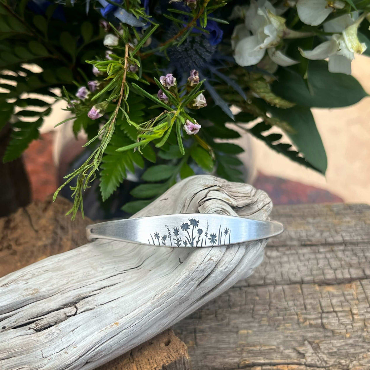 Wildflowers Signet Cuff displayed on driftwood with wildflowers in background.