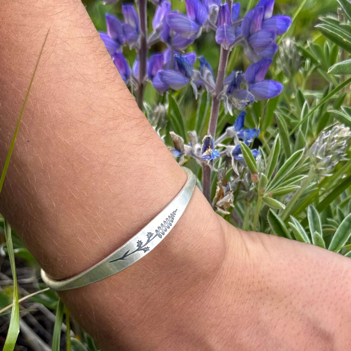Lupine Flower Cuff Bracelet worn on wrist among blooming lupine flowers in a natural setting.