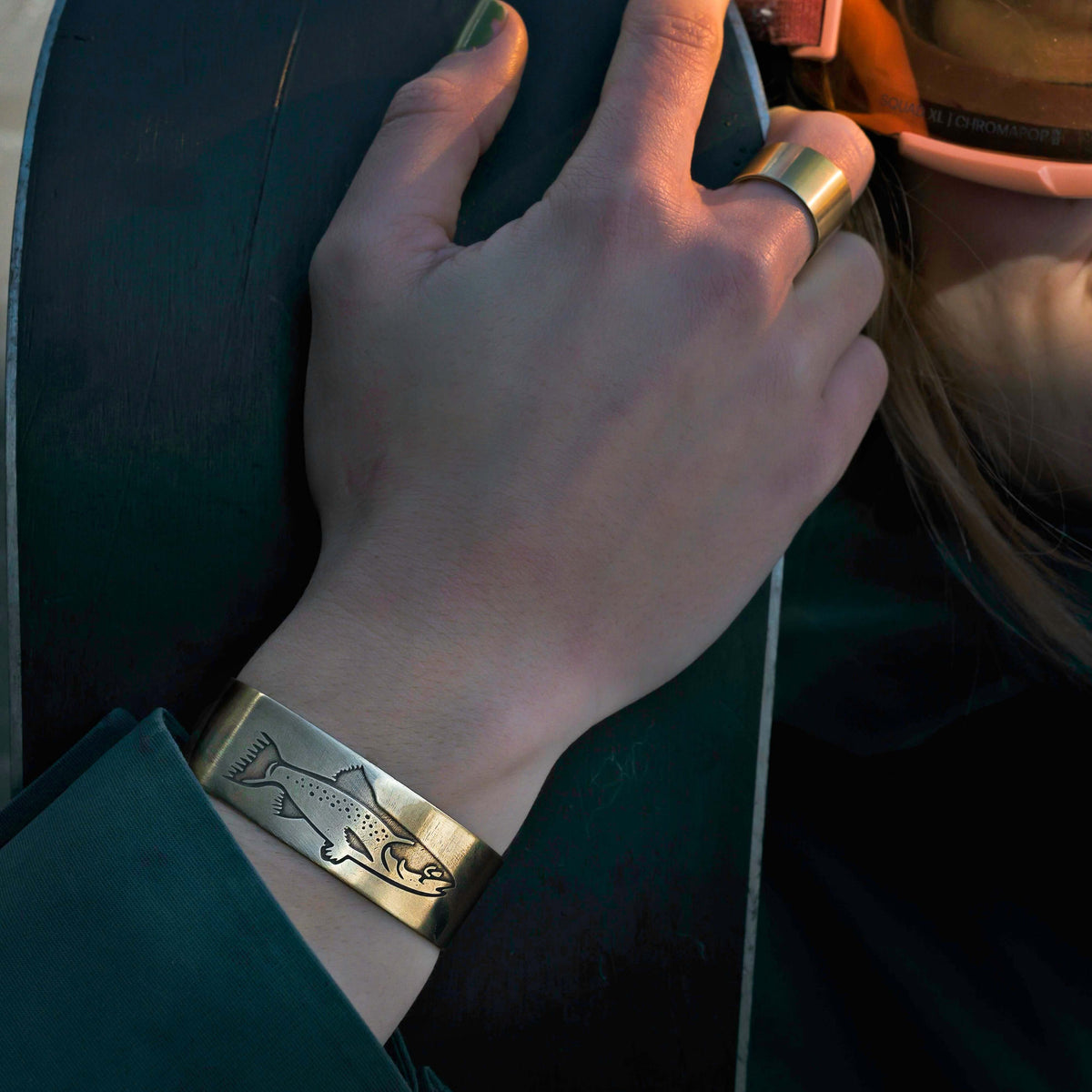 Steelhead Cuff Bracelet featuring an engraved steelhead design in antique brass on a women's wrist