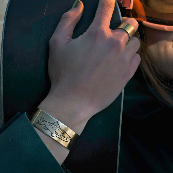 Steelhead Cuff Bracelet featuring an engraved steelhead design in antique brass on a women's wrist
