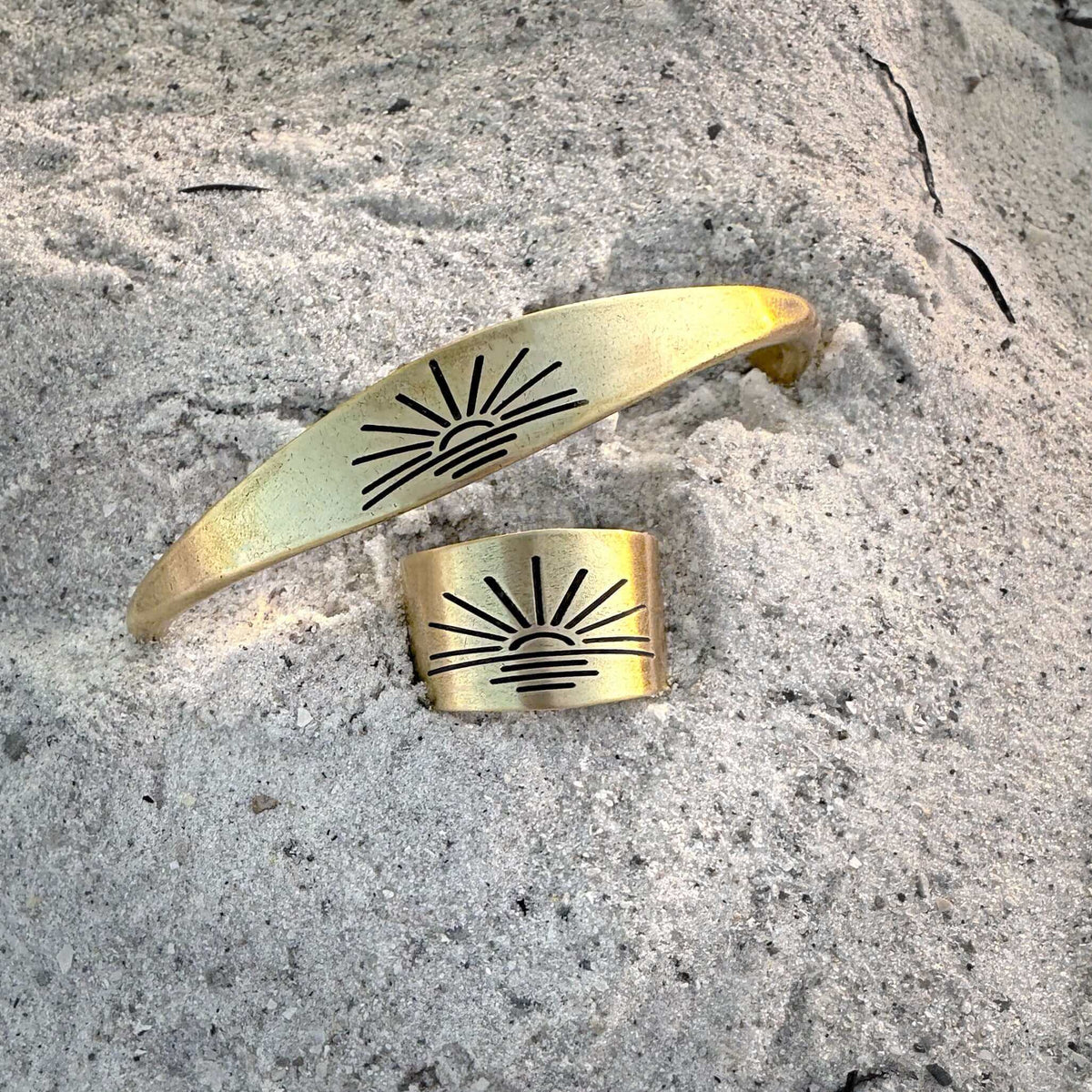 Sunrise Signet Cuff in antique brass finish displayed on sandy surface.