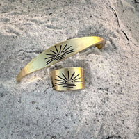 Sunrise Signet Cuff in antique brass finish displayed on sandy surface.