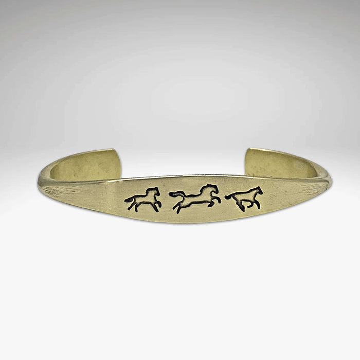 Wild Horses cuff bracelet in antique brass showcasing galloping horse designs, elegant and timeless jewelry piece.