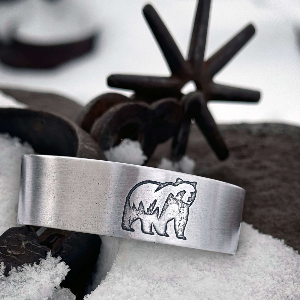 Griz Cuff Bracelet featuring a grizzly bear silhouette, on antique steel machine in the snow