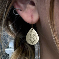 Teardrop-shaped earrings featuring a detailed paintbrush flower design in antique brass finish, worn elegantly.