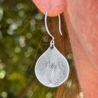Petals Earrings in matte silver, featuring a delicate floral design, worn by a model against a blurred natural background.