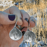 Hand holding floral-inspired Petals Earrings in Matte Silver, showcasing intricate petal design against natural backdrop.