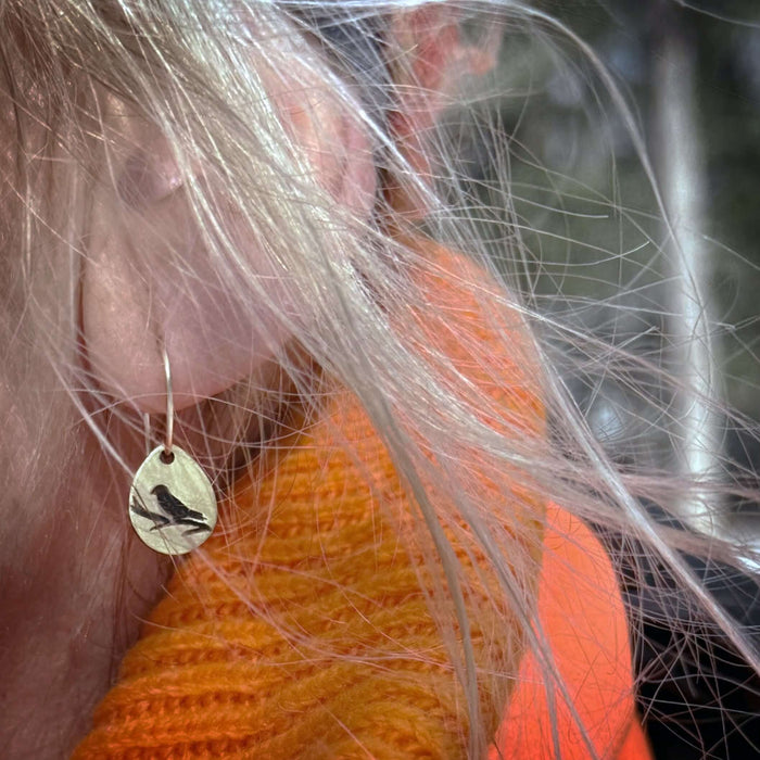 Mountain Bluebird Earrings featuring a teardrop design with a bird silhouette, worn by a person with long blond hair.