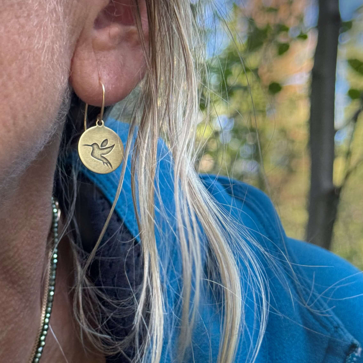 Antique brass hummingbird earrings worn by a woman outdoors, perfect for bird lovers and nature enthusiasts.