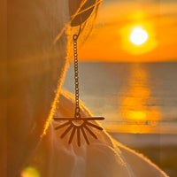 Sunbeam Earrings featuring delicate sunray design, swinging on a rolo chain against a sunset backdrop.