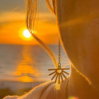 Close-up of Sunbeam Earrings glistening in sunset light, featuring delicate sun ray design on chain.