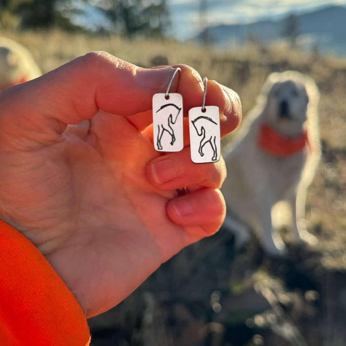 White Horse Dressage Earrings held in hand, featuring etched horse silhouettes on brass, ideal for equestrians.