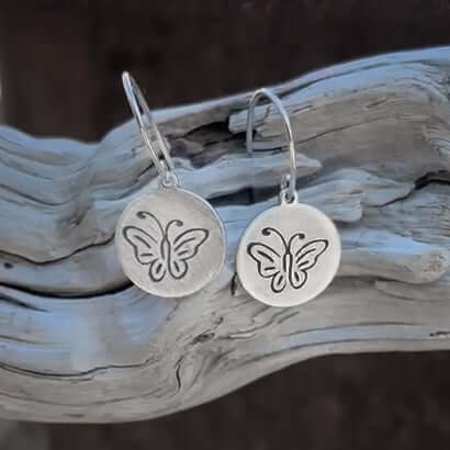 A simple butterfly design on a small round disc with sterling silver earwires on a aged piece of wood.