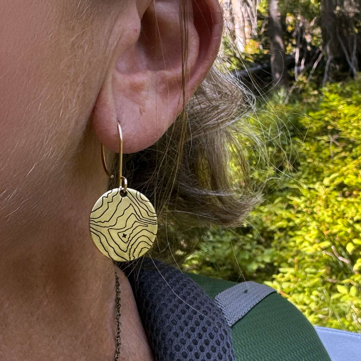 Rising Wolf Earrings showcasing a topographic design hanging on a model's ear in nature.