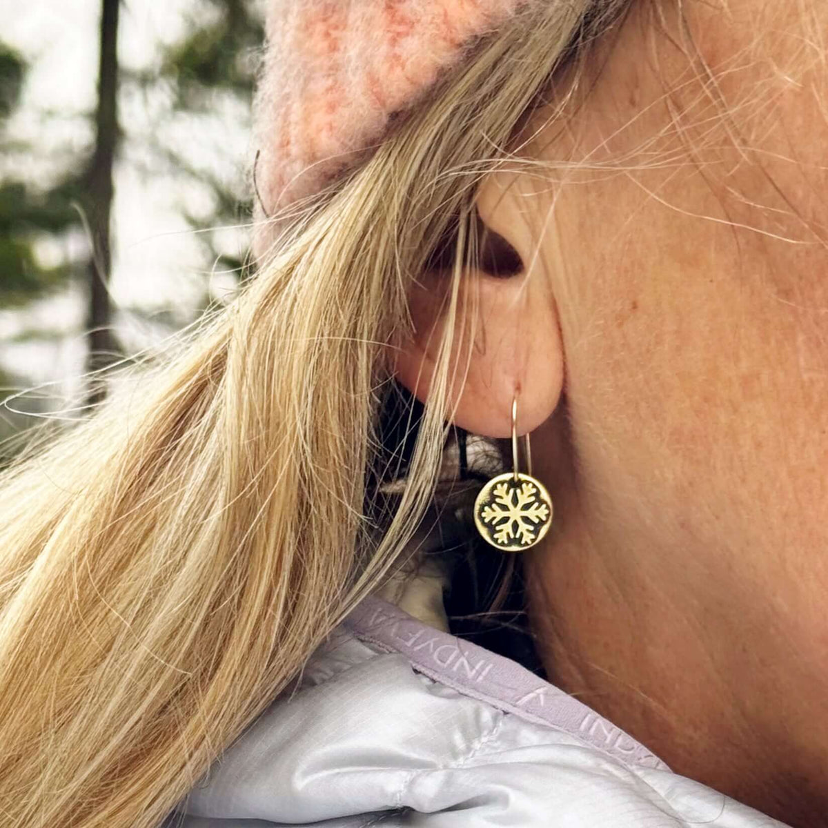 Close-up of a woman wearing Powder Snowflake Earrings, showcasing the gold etched snowflake design on a disc.