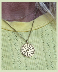 Antique brass Bitterroot pendant on a gold plated chain on a woman with a yellow sweater.