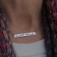 Close-up of the Antler Bar Necklace showcasing its sleek design and acid-free etching, worn with a colorful scarf.