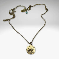 Antique brass circular pendant with a running fox and full moon, stars and a mountain background.