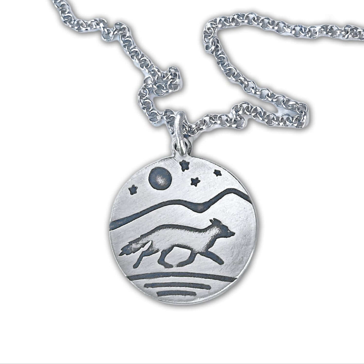 Circular pendant with a running fox and full moon, stars and a mountain background.