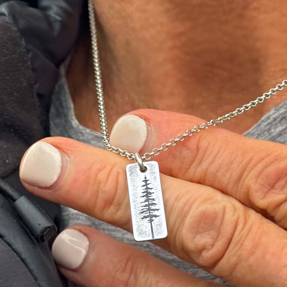 Close-up of a hand holding a silver Pine Tree Necklace with a Ponderosa pine design on the pendant.