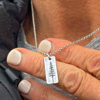 Close-up of a hand holding a silver Pine Tree Necklace with a Ponderosa pine design on the pendant.