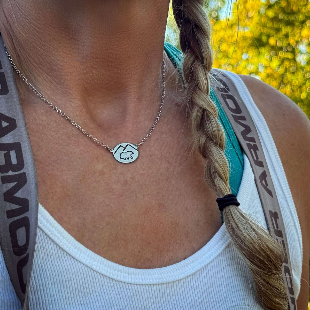 Close-up of a Mountain Bear Necklace, featuring a silver pendant with mountain design, worn by a woman outdoors.