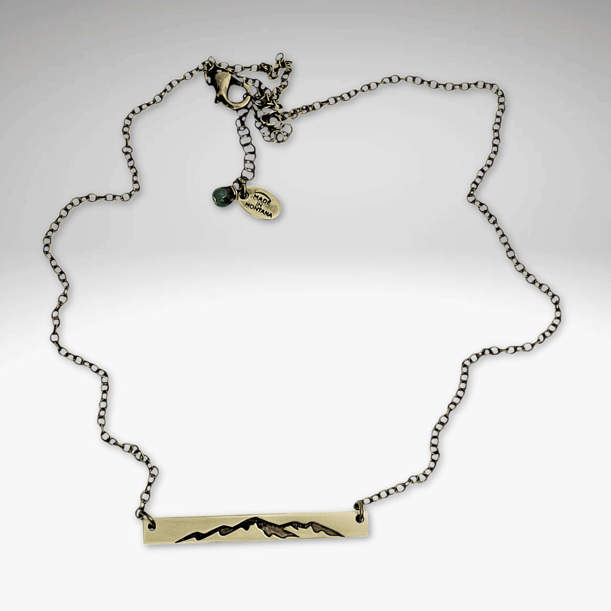Mountainscape Necklace featuring a raw brass bar with etched mountain silhouette on an adjustable chain.