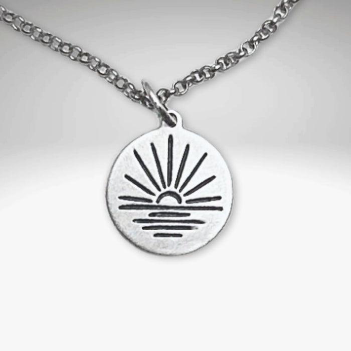 Sunrise Necklace with silver pendant featuring a sunrise over water, adjustable chain length, elegant jewelry piece.