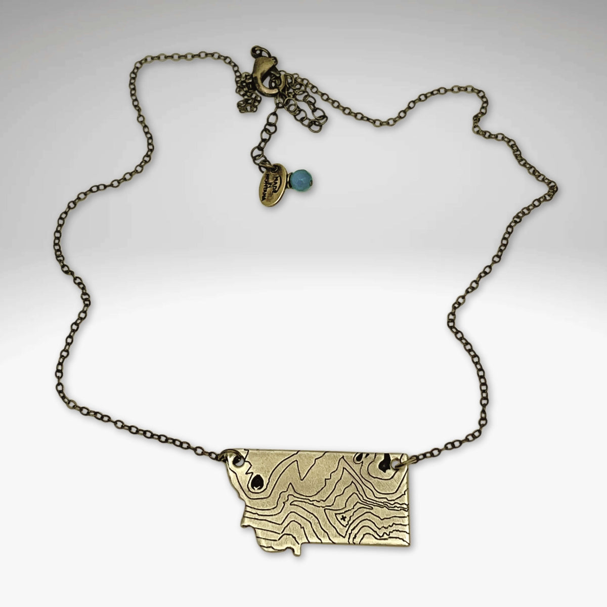 Rising Wolf MT Necklace - Topo Montana showcasing a topographic design with a rising wolf and Montana mountains.
