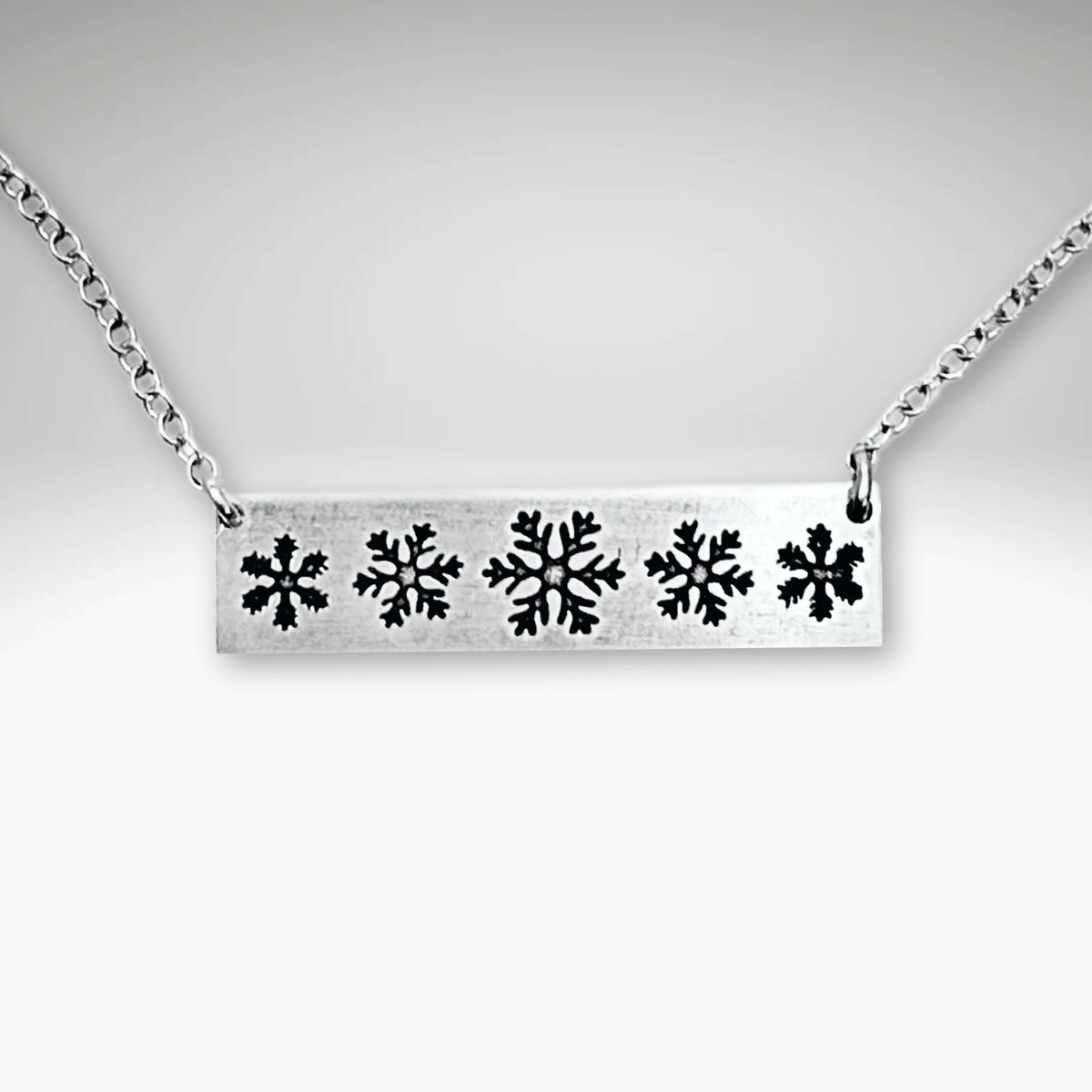 Snowfall Necklace featuring a silver bar with intricate snowflake design on a chain, perfect accessory for winter lovers.