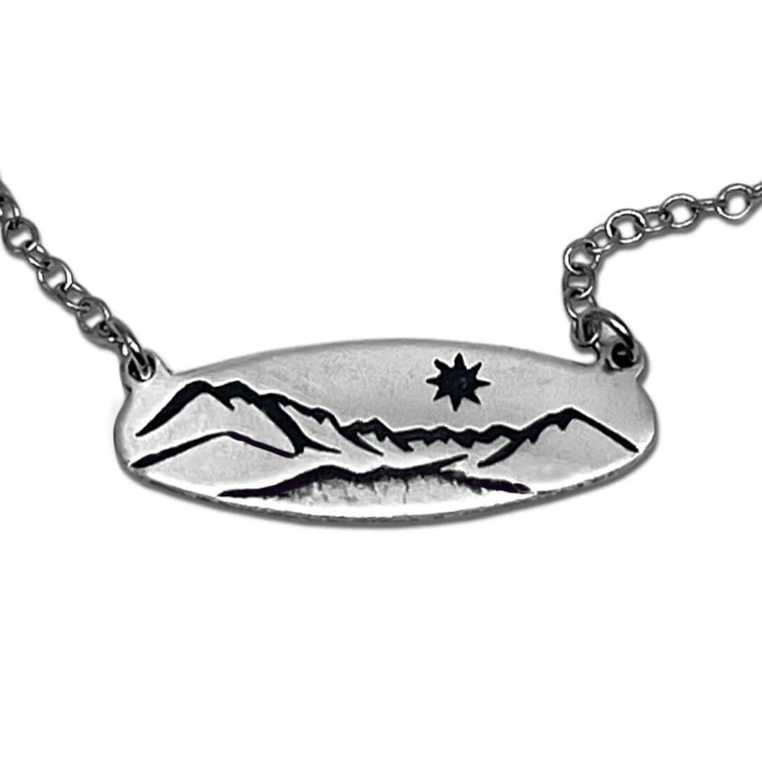 Glacier View Necklace featuring a hand-engraved mountain design in matte silver, showcasing a star detail.