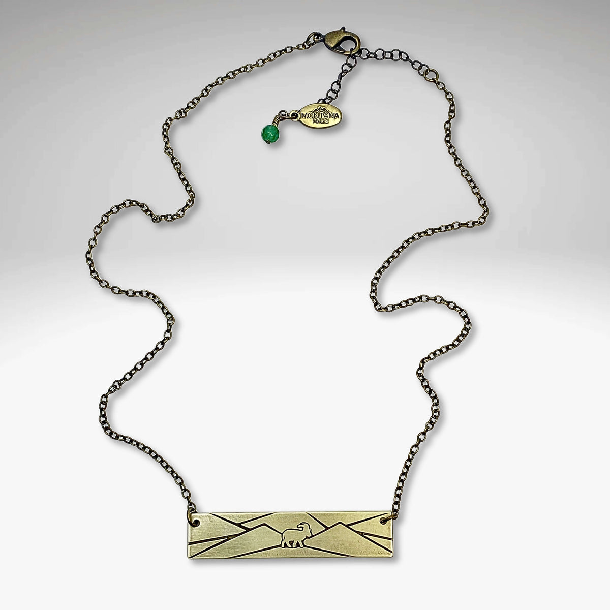 Mountain goat necklace in antique brass finish on a delicate chain with green accent bead, perfect for nature lovers.