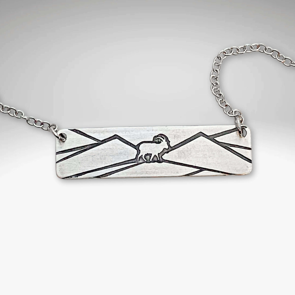Mountain goat necklace in matte silver on a rolo chain, showcasing a minimalist mountain design.