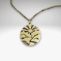 Going to the Sun Necklace featuring a mountain pendant with sunburst design on an antique brass chain.