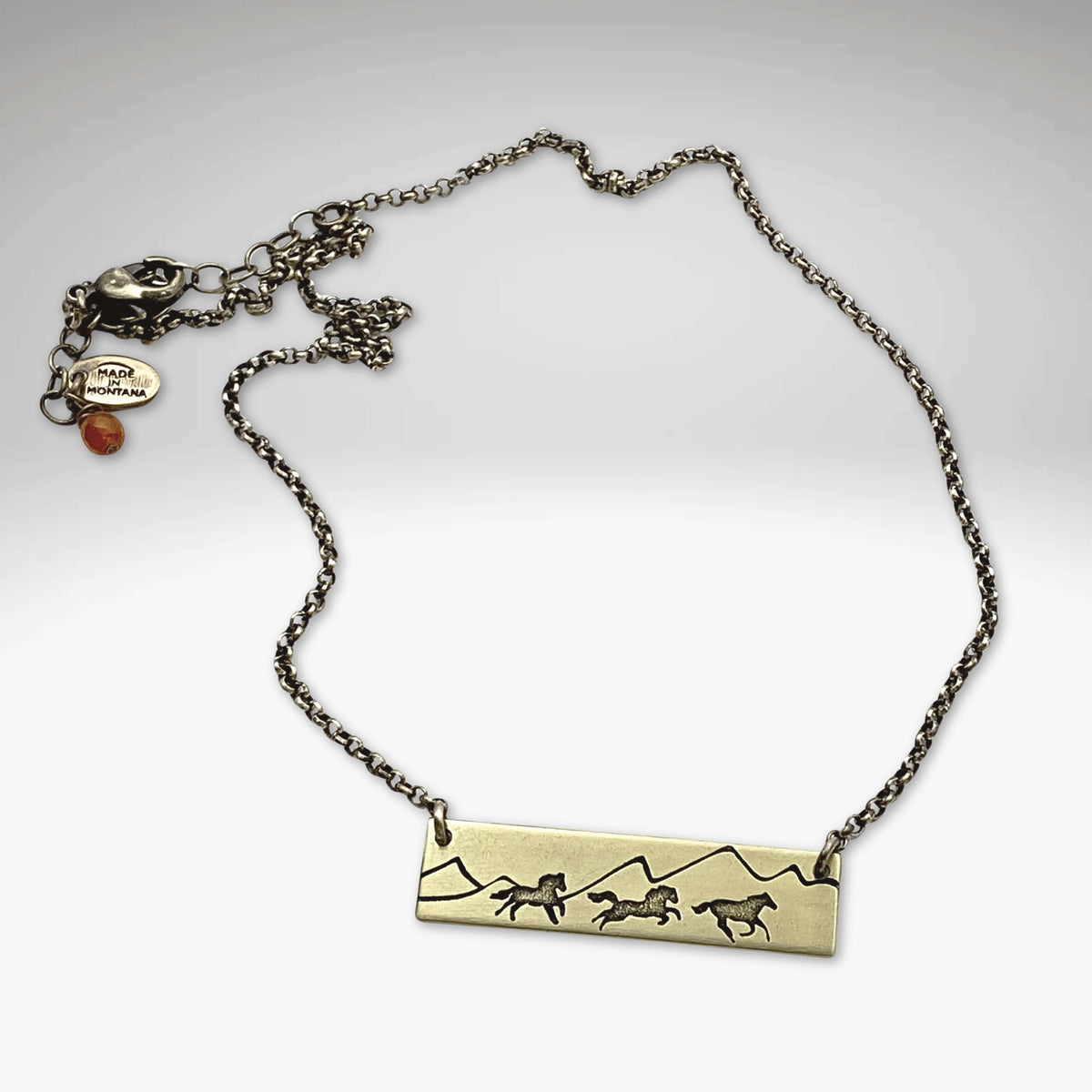 Wild Horses Necklace featuring a brass pendant with etched wild horses and mountains, paired with a dainty chain.