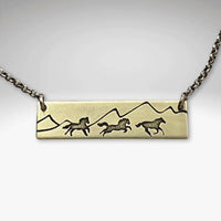 Wild Horses Necklace featuring brass etching of running horses and mountain silhouette on a chain.