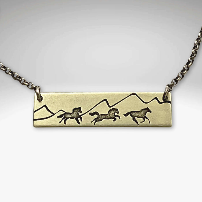 Wild Horses Necklace featuring brass etching of running horses and mountain silhouette on a chain.