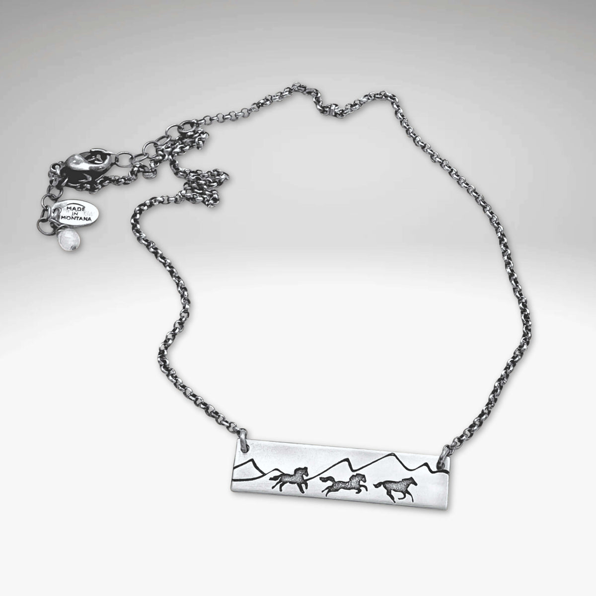 Wild Horses Necklace featuring etched mountains and mustangs on a silver chain, symbolizing freedom and the wild west.