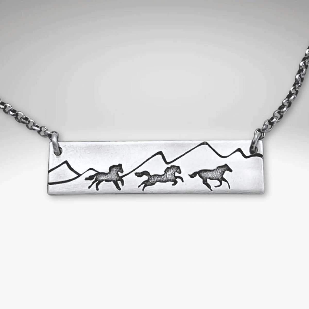 Wild Horses Necklace with etched mountains and galloping horses on a silver chain.