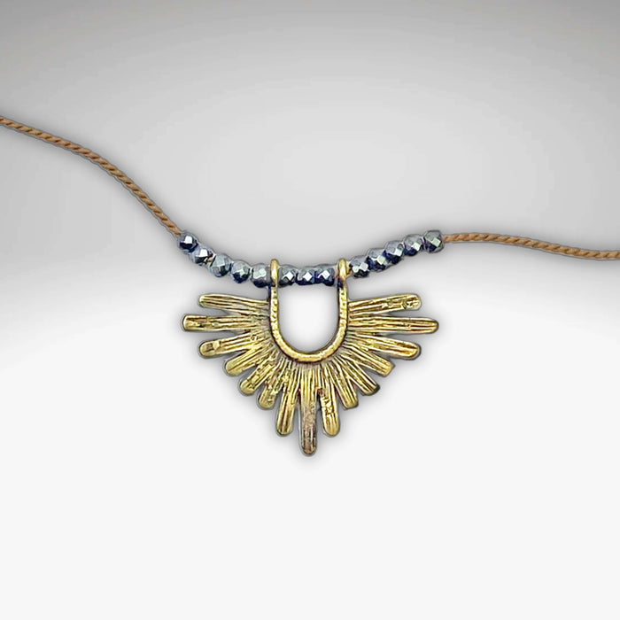 Sunbeam Necklace featuring a geometric gold pendant on a silk cord with crystalline hematite beads, adjustable length.