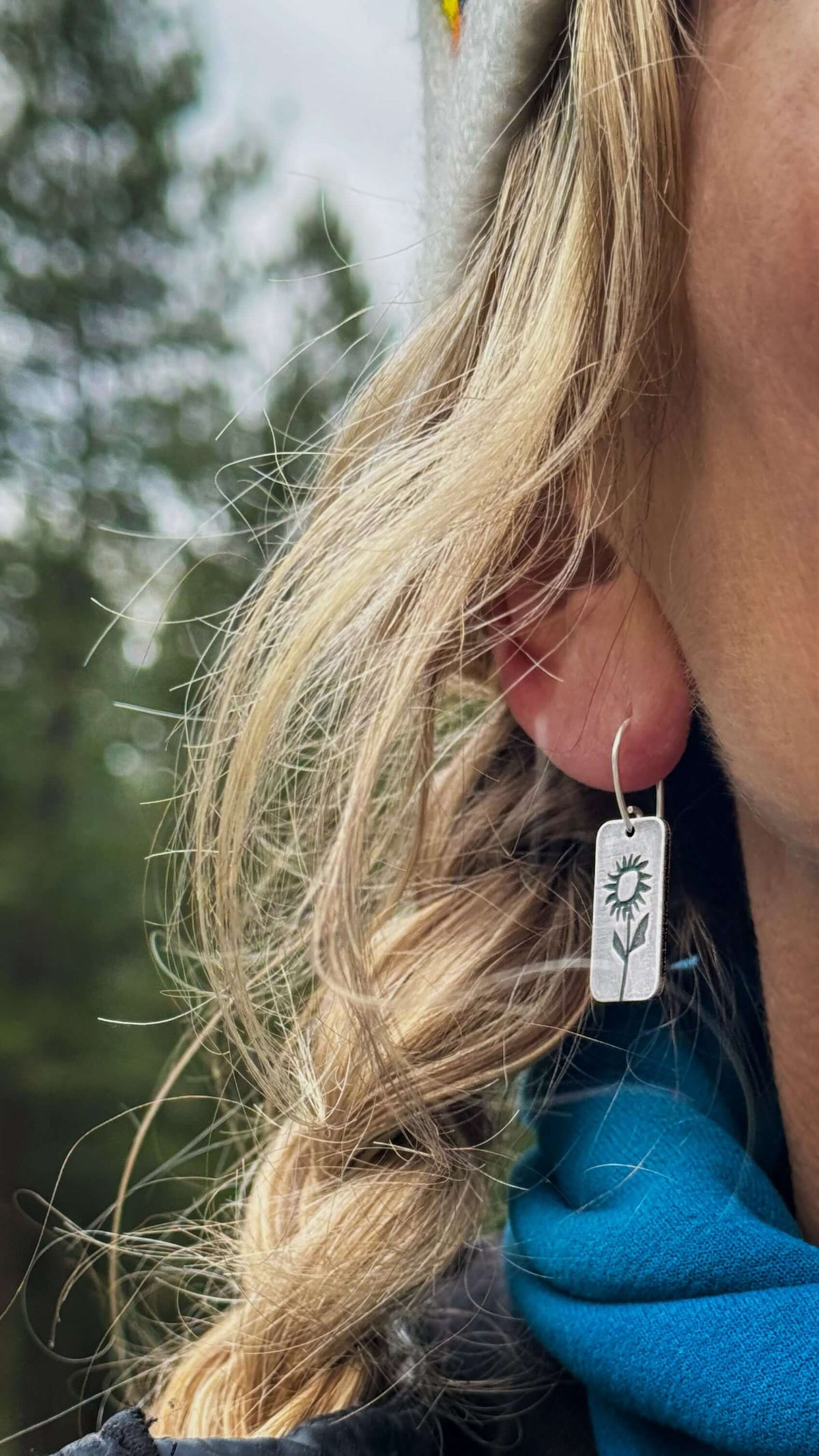 Balsamroot flower earrings in matte silver worn by a woman outdoors, showcasing nature-inspired design.