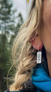 Balsamroot flower earrings in matte silver worn by a woman outdoors, showcasing nature-inspired design.