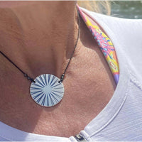 Ray Necklace with sun ray design worn on a person, featuring a black cord and bright circular pendant.