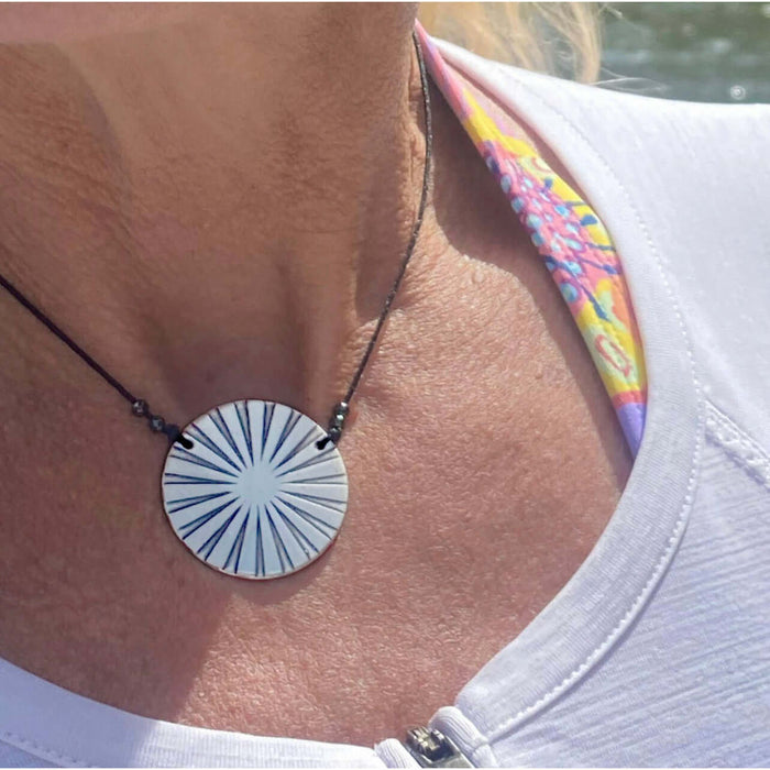 Ray Necklace with sun ray design worn on a person, featuring a black cord and bright circular pendant.