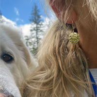 Close-up of Flyover Earrings featuring a bird design, worn by a person with a white dog nearby.